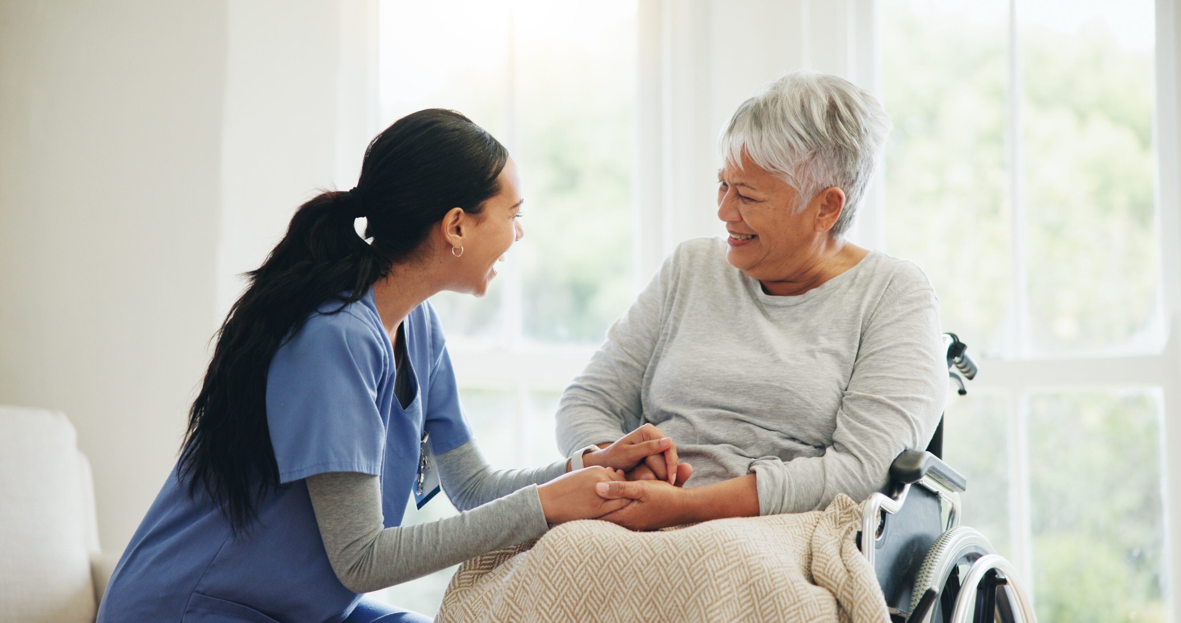 A nurse and elderly woman smiling and holding hands.
